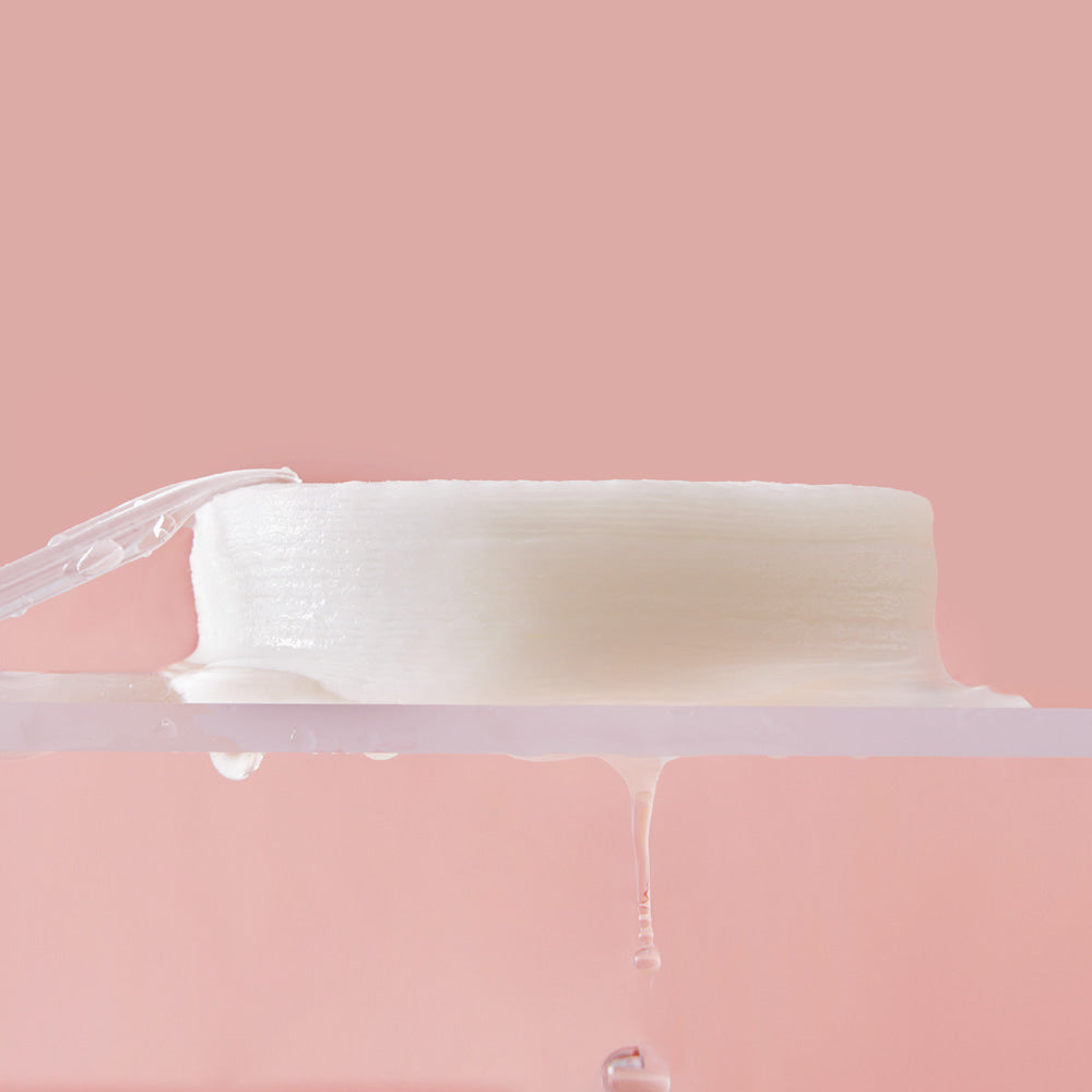 Close-up of a white soap bar with clear liquid on a pink background